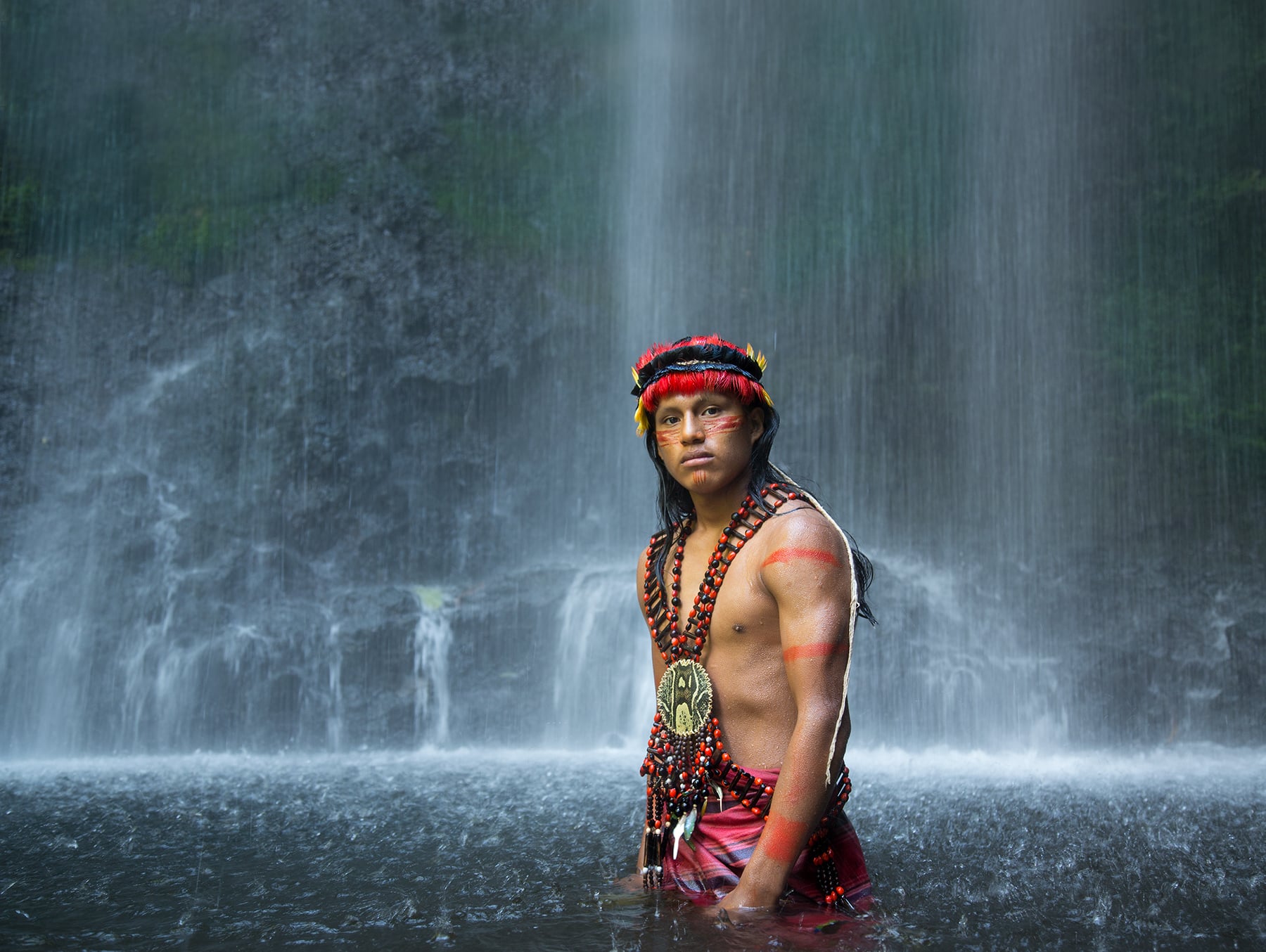 the Amazonian river leading to the waterfall that is the backdrop in this image is deeply understood by this Shuar warrior. Amazon.