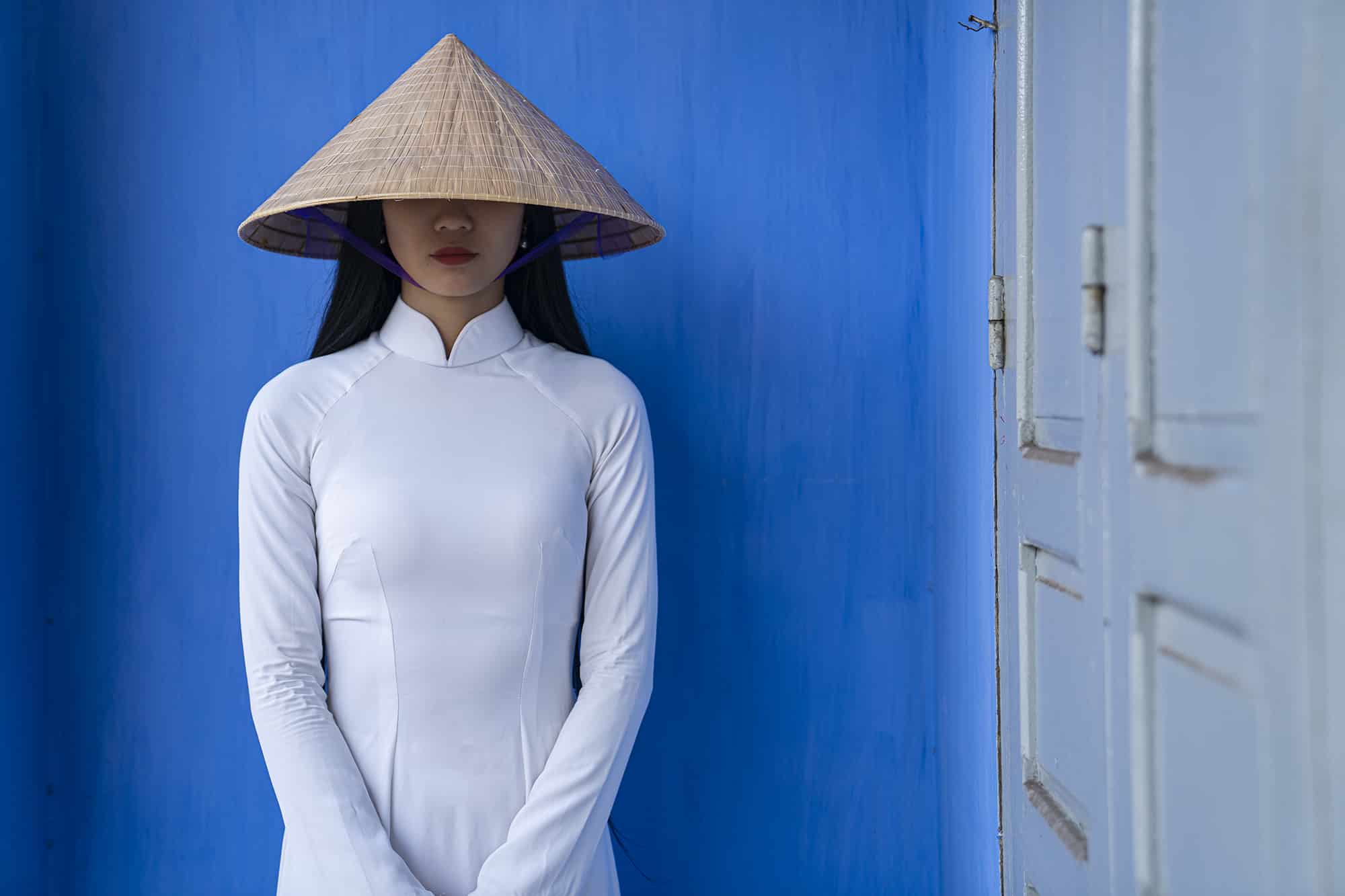 Women covering her eyes standing in front of a blue wall in Vietnam