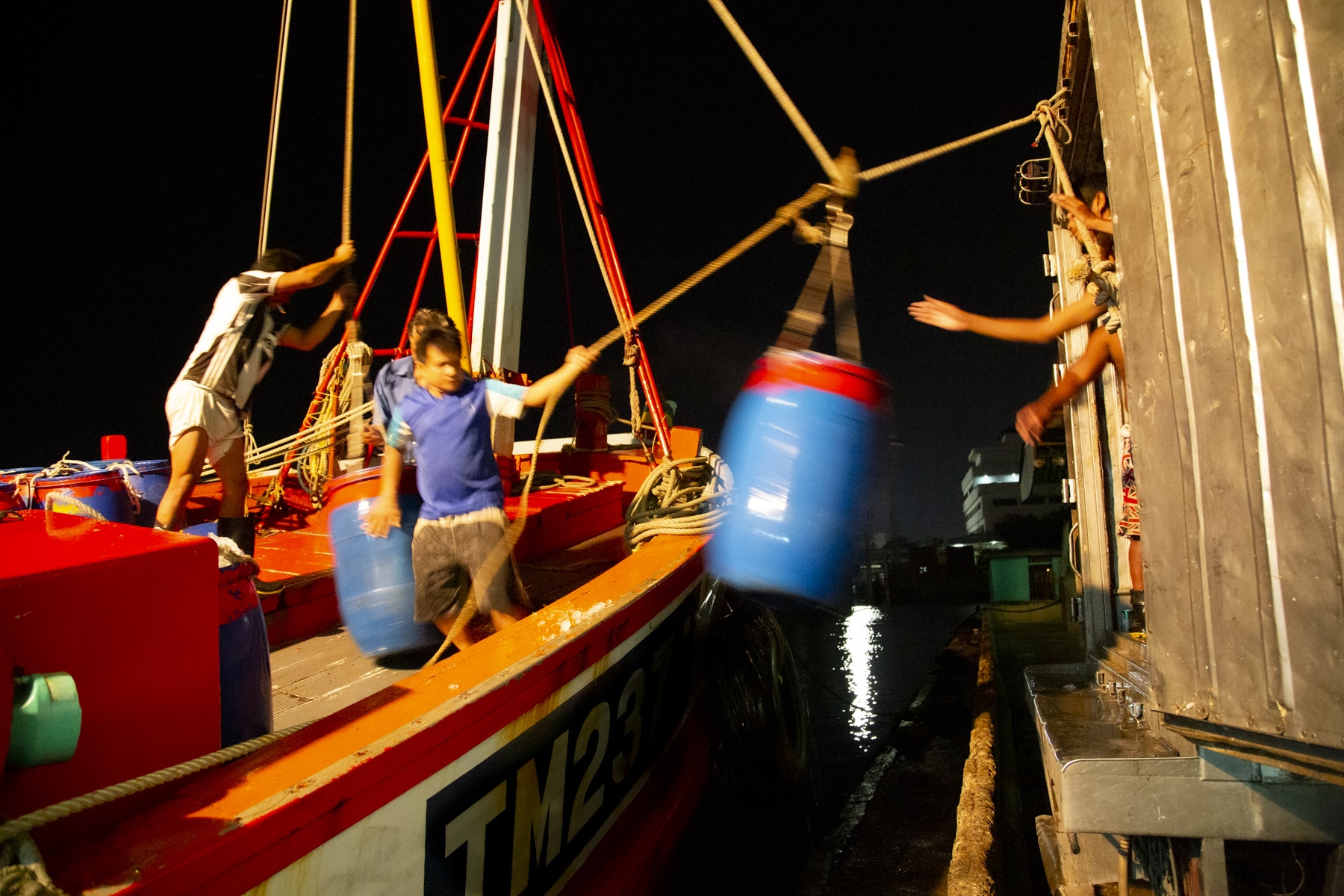 Workers passing barrels from boat to shore in Thailand