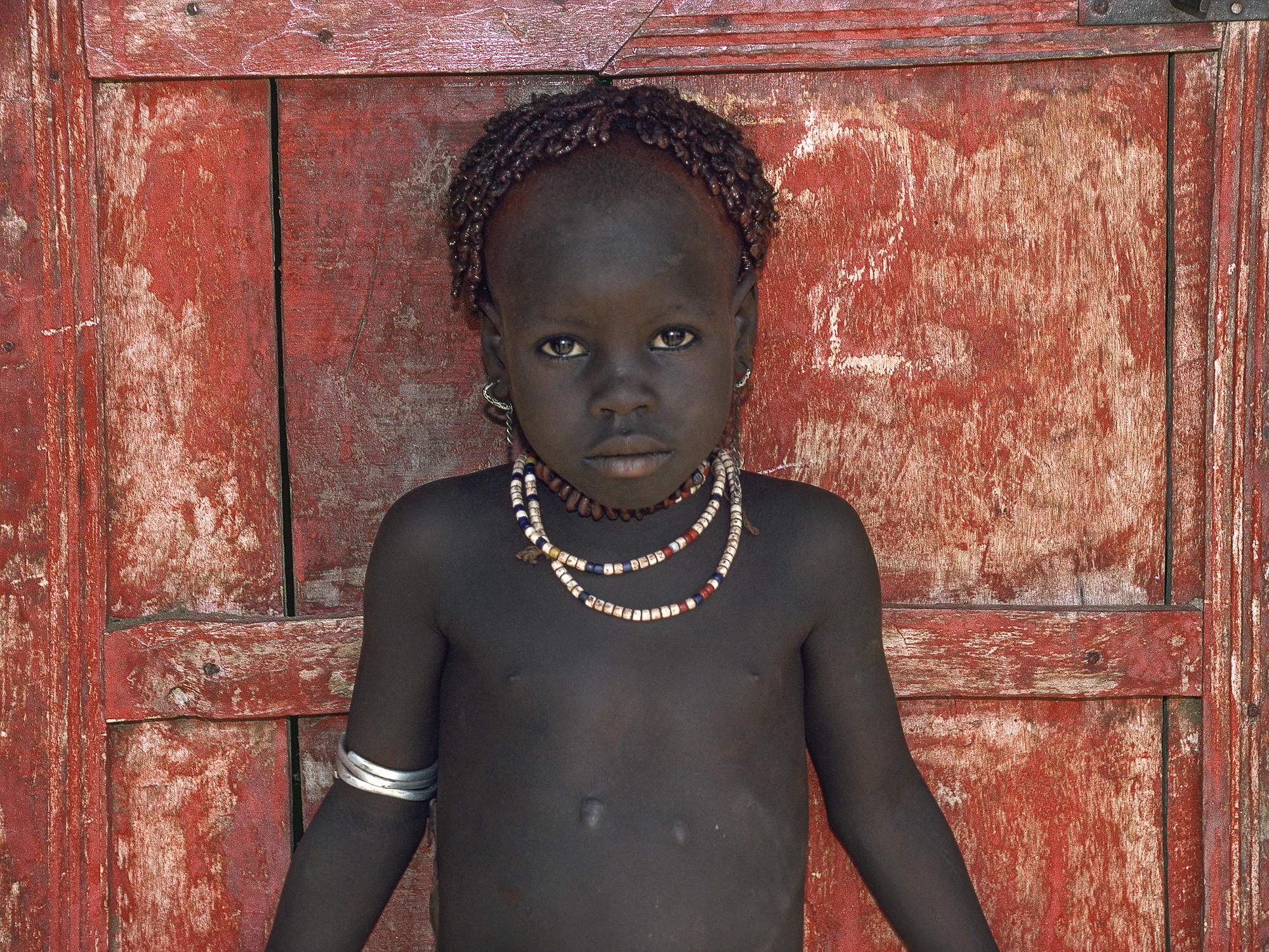 Child standing in front of a red door in Ethiopia
